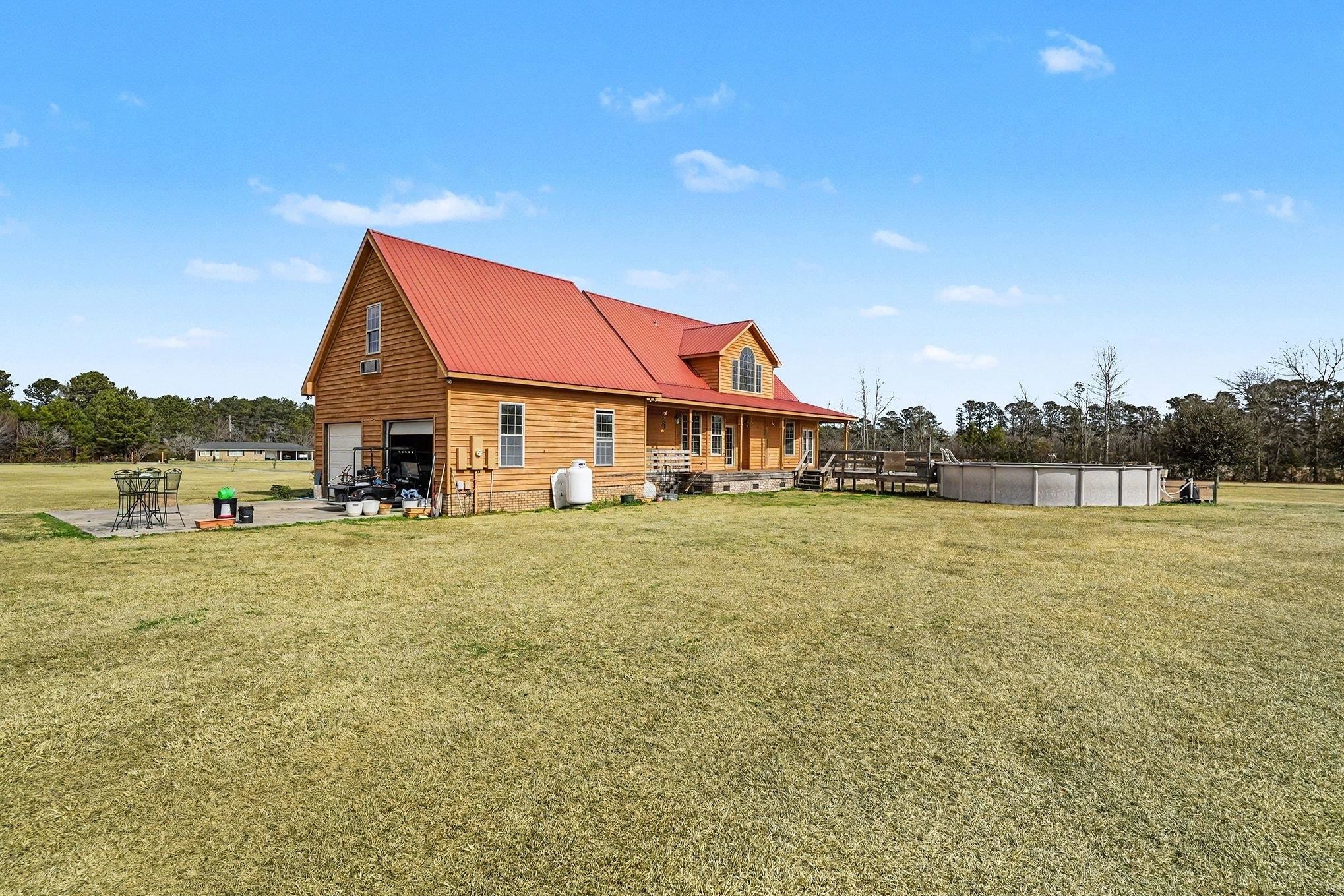 202 Highway 747 Loris Sc 29569 Loris, SC 29569 - Photo 26 of 34 Rear view of property featuring a garage, a lawn, a metal roof, an outdoor pool, and a porch