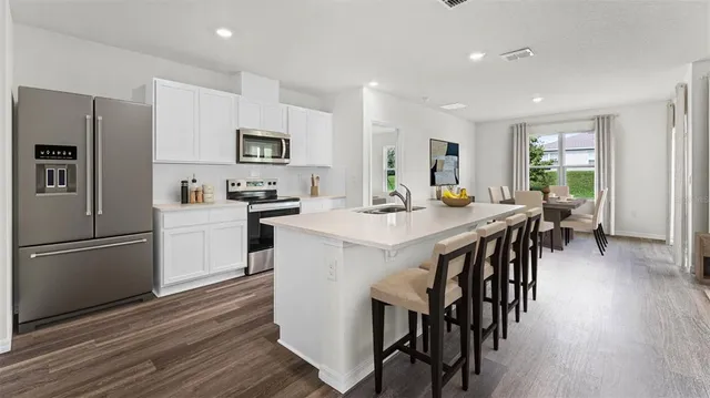 a kitchen with stainless steel appliances kitchen island granite countertop a refrigerator a stove a sink a dining table and chairs with wooden floor