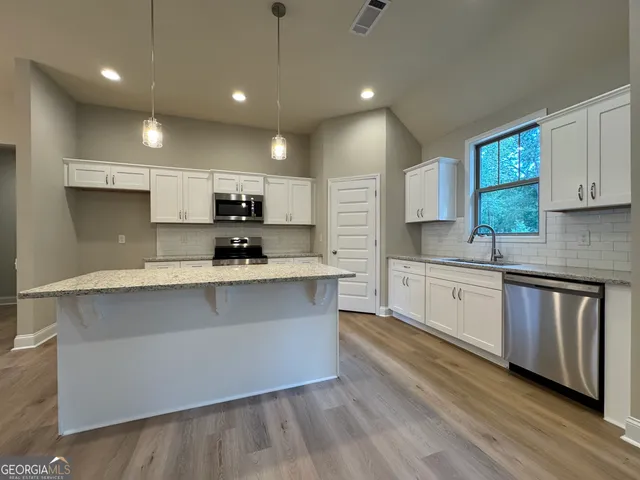 a large kitchen with stainless steel appliances a large counter top a stove a sink cabinets and a wooden floor