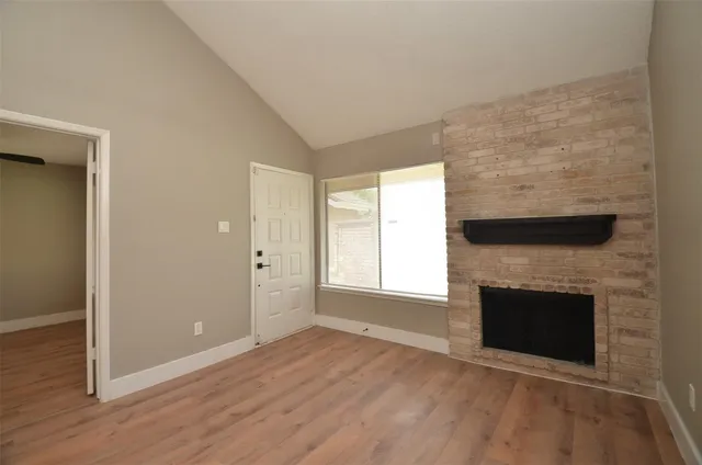 an empty room with wooden floor fireplace and windows