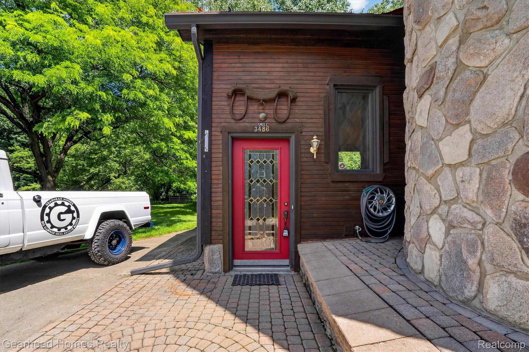 3486 West Drahner Road Oxford, MI 48371 - Photo 6 of 51 Stone and wood-sided exterior featuring a red entry door with decorative glass