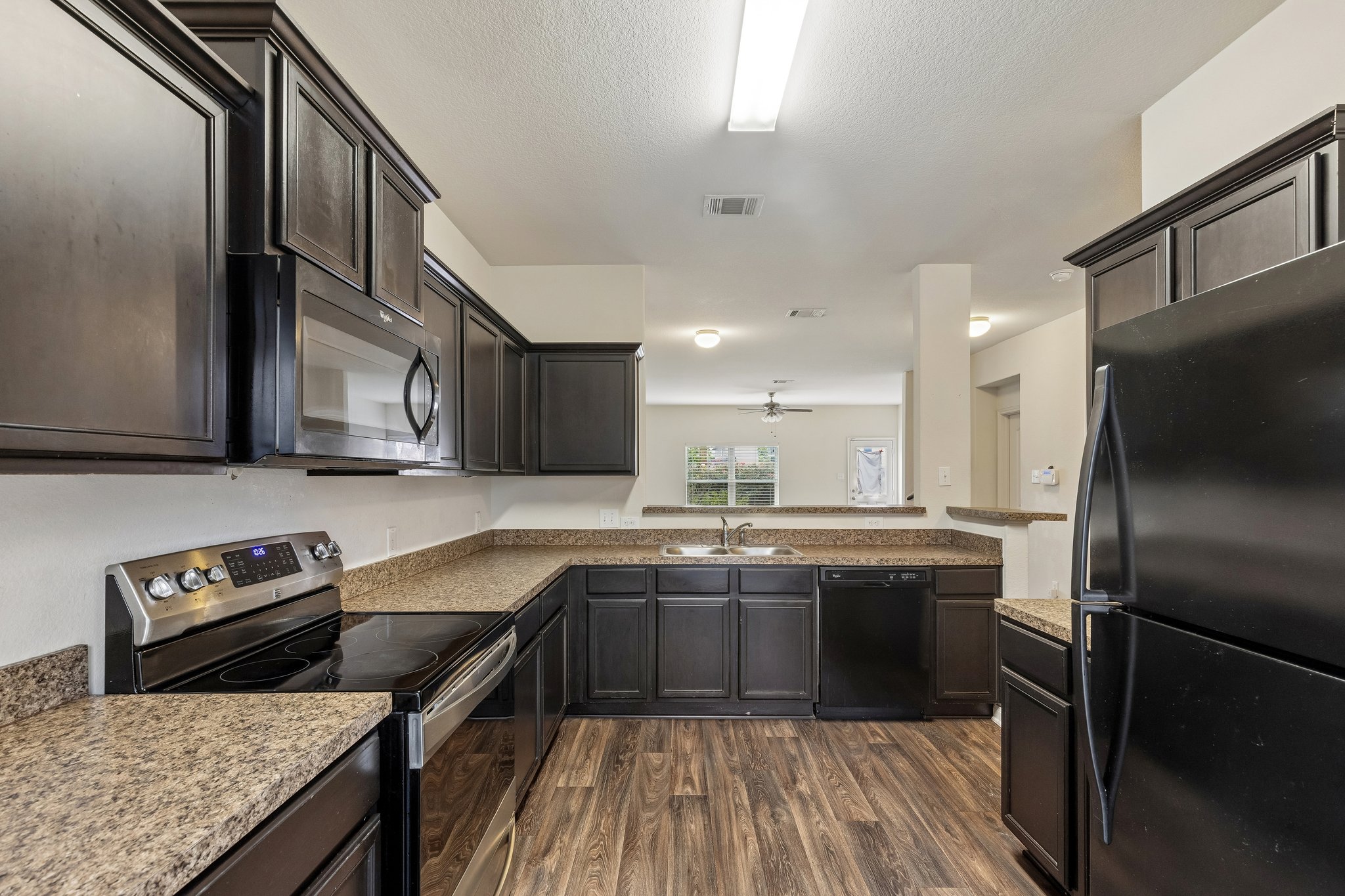 704 Cleary Lane Jarrell, TX 76537 - Photo 2 of 25 Kitchen featuring dark wood-finish cabinetry, granite-style countertops, wood-finish flooring, a stainless steel range, and an over-range microwave
