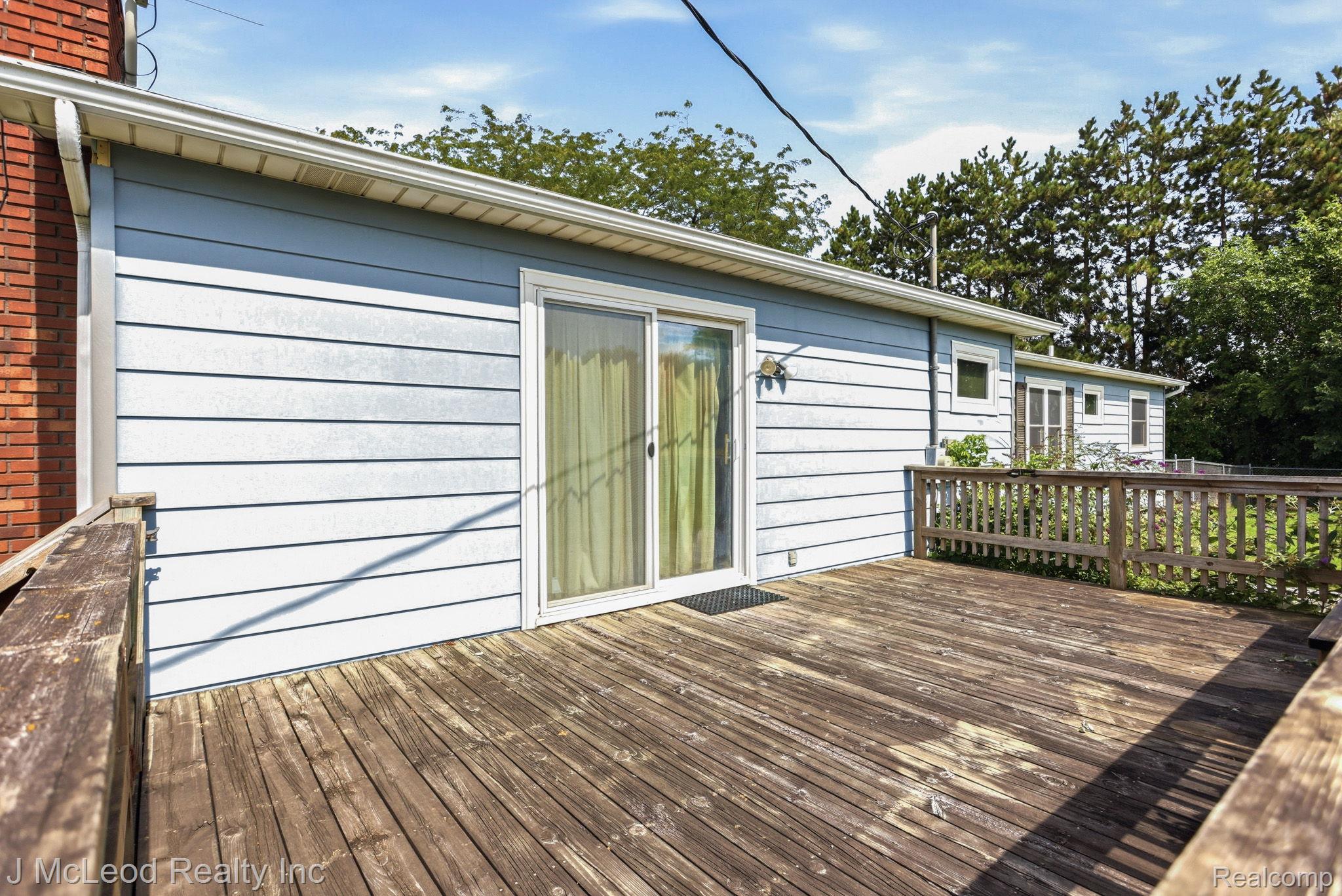9481 Swaffer Road Vassar, MI 48768 - Photo 31 of 39 Expansive wood deck with a full railing, featuring a sliding glass door entry to the building, light blue horizontal siding, and a brick exterior wall
