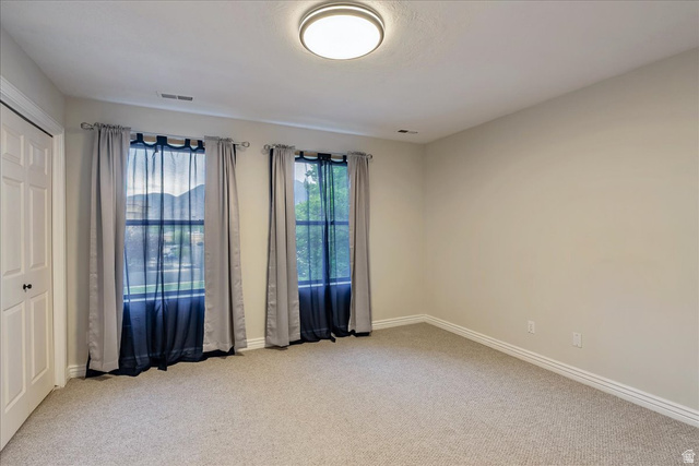 38 South 1000th Street East Payson, UT 84651 - Photo 17 of 19 Neutral tone walls with light-colored carpet, featuring two windows with mountain scenery, a white paneled door, and a flush-mount ceiling light fixture