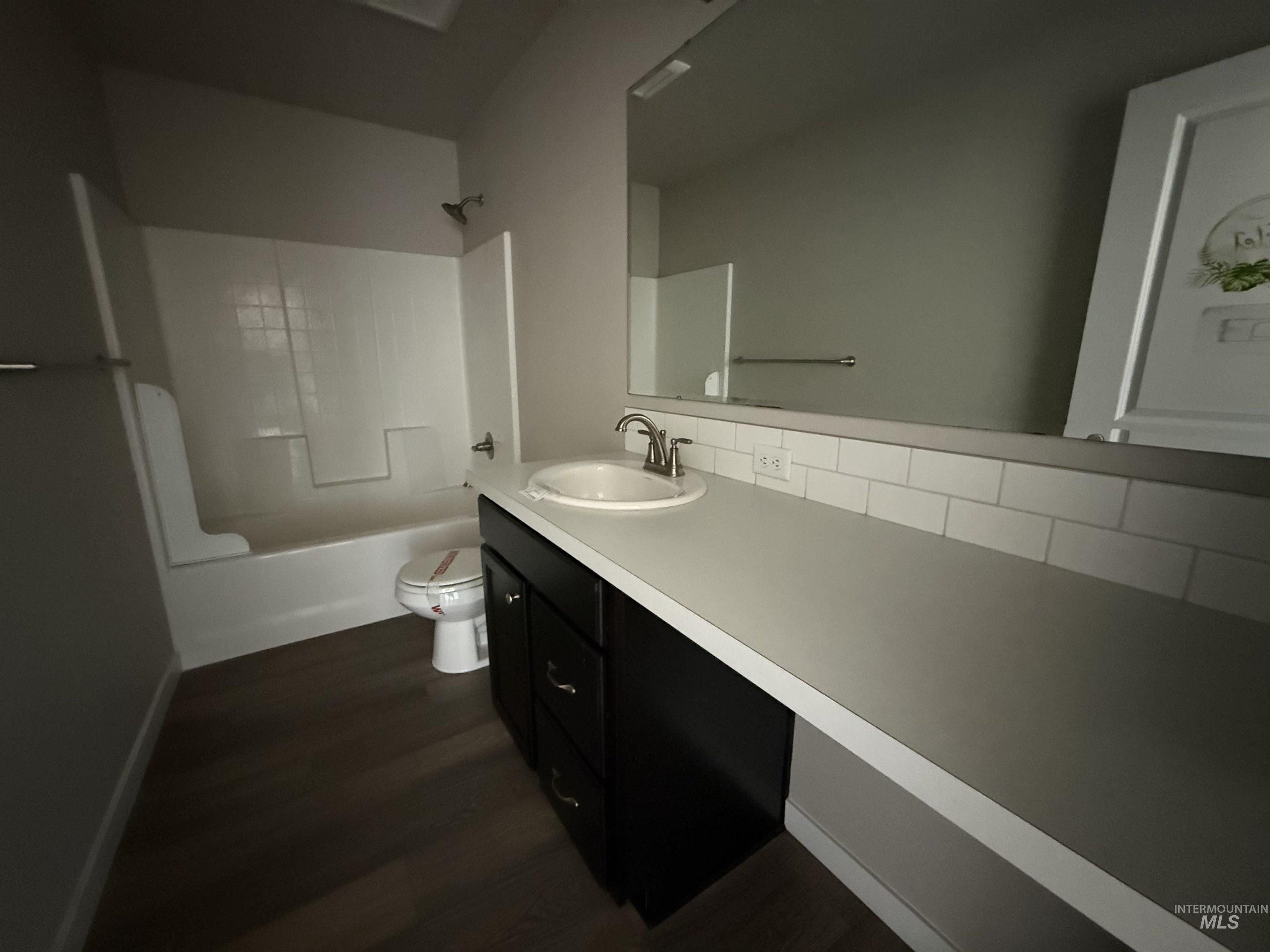 12451 Varga Street Caldwell, ID 83607 - Photo 7 of 30 Wood-finish flooring, dark wood vanity with ample storage, white subway tile backsplash, integrated sink with chrome faucet, and white tub/shower combination