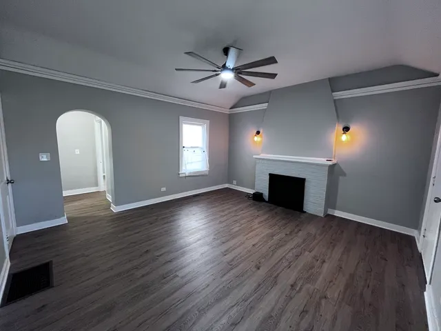 an empty room with wooden floor a ceiling fan a fireplace and windows