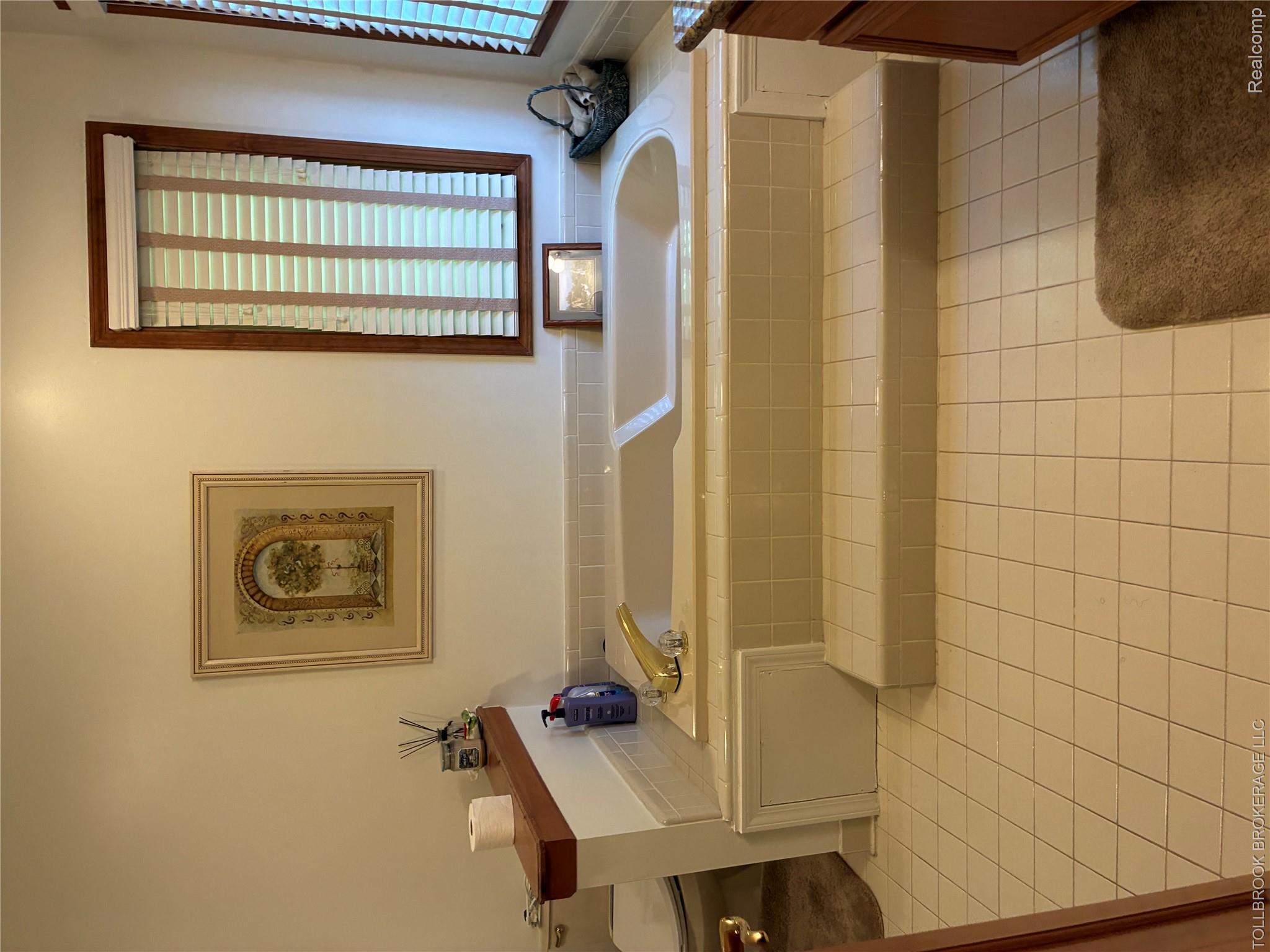 6187 Country Ridge Drive Troy, MI 48098 - Photo 18 of 23 Recessed soaking tub with tiled surround and steps, large window with wood trim, and square tile flooring
