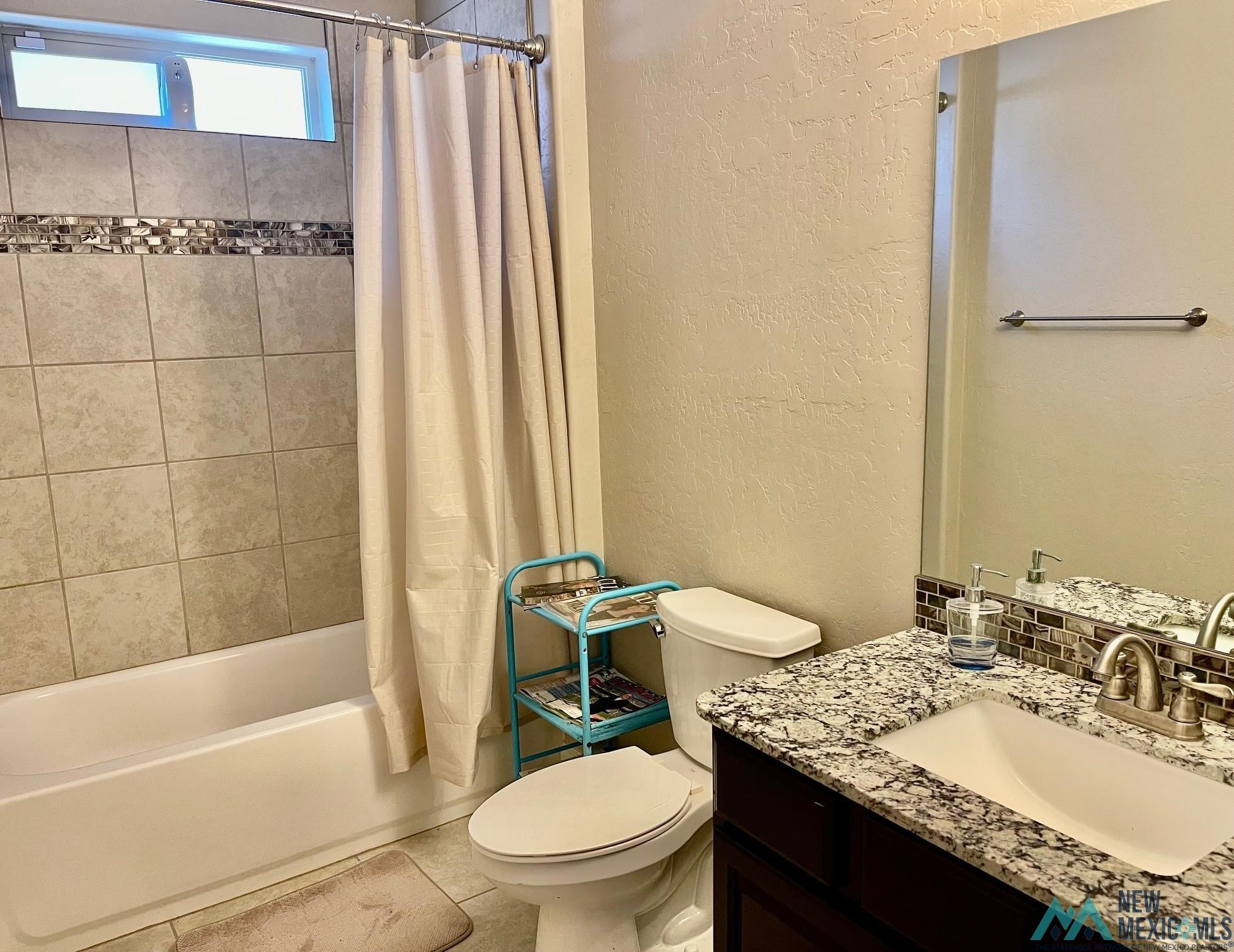 Bathroom with a textured wall, shower / bathtub combination with curtain, vanity, and backsplash