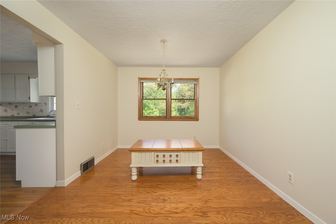 6600 Peck Road Ravenna, OH 44266 - Photo 8 of 50 Unfurnished dining area with light wood-style floors, a textured ceiling, and a chandelier