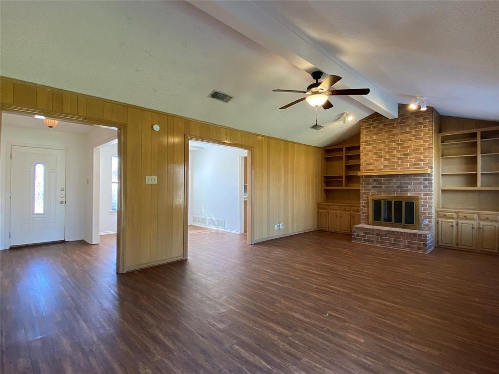 an empty room with wooden floor a ceiling fan a fireplace and windows