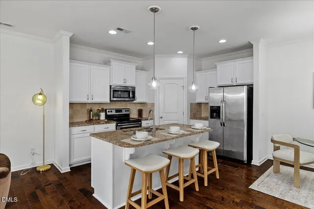 a kitchen with stainless steel appliances granite countertop a refrigerator a stove a sink a dining table and chairs with wooden floor