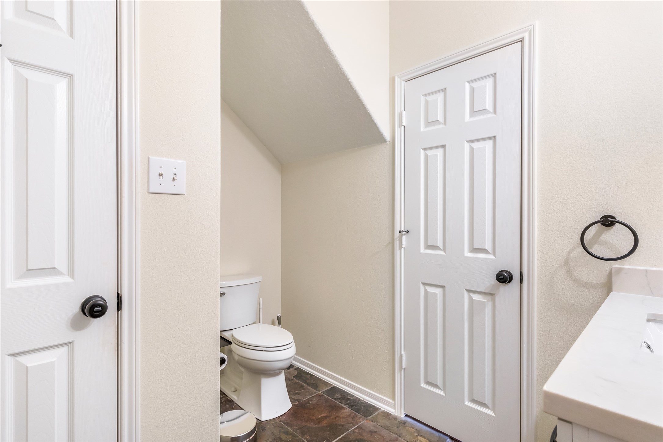 12122 Landsdown Ridge Way Humble, TX 77346 - Photo 19 of 34 This is a small bathroom featuring a toilet under a sloped ceiling, neutral walls, and tile flooring. It includes a quartz countertop with a sink, a towel ring, and two entrance doors.