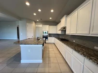 a large kitchen with kitchen island granite countertop a stove a sink and a white counter space