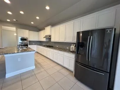 a large kitchen with granite countertop a refrigerator and a stove top oven