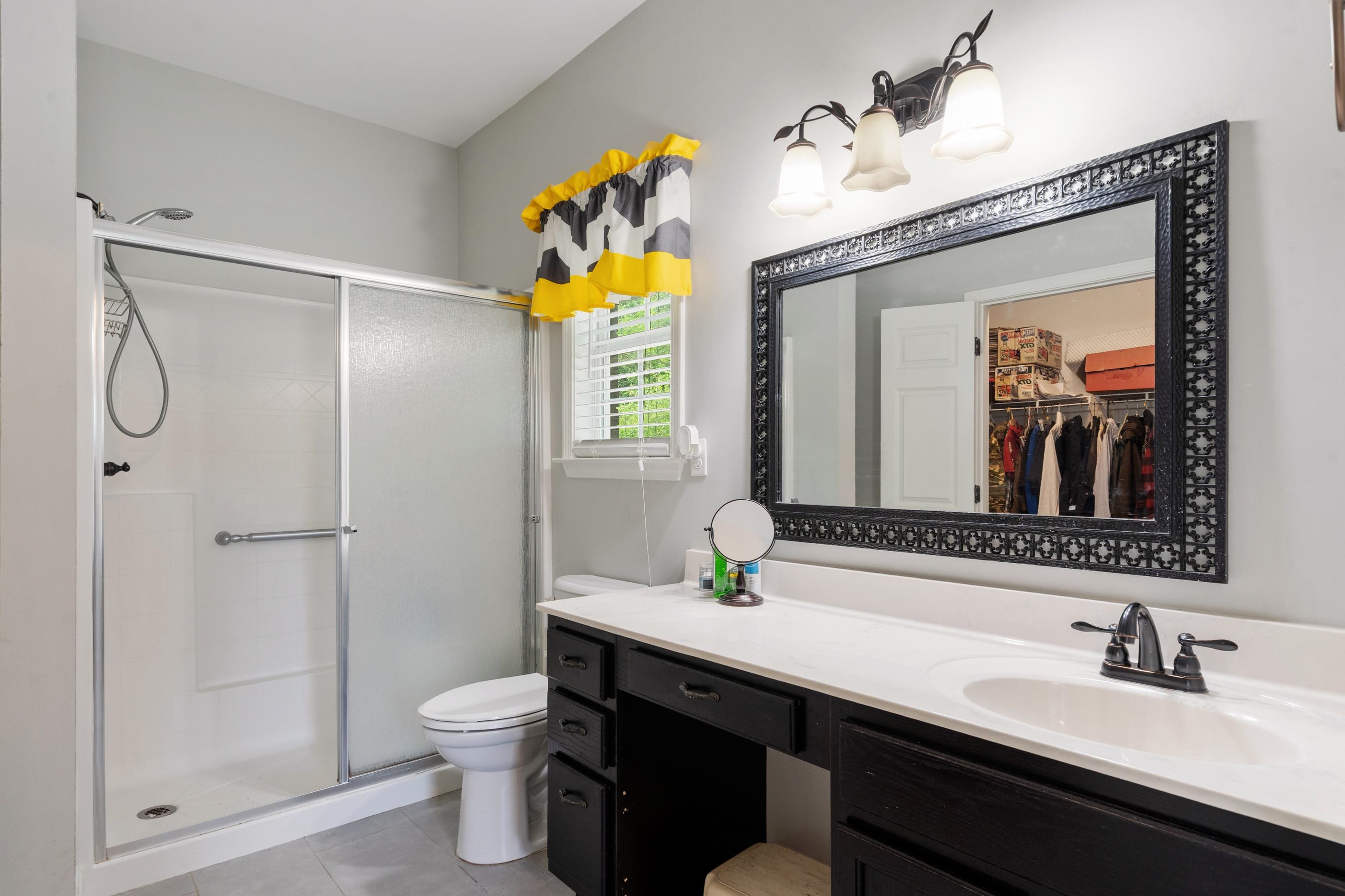 7757 Brunswick Road Millington, TN 38053 - Photo 29 of 40 Bathroom featuring a shower with sliding glass doors, a single vanity with a white countertop and dark cabinetry, a vanity mirror with an ornate dark frame, and a three-light fixture