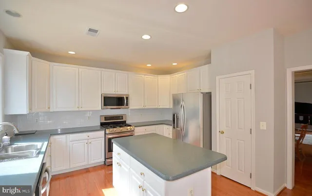 a kitchen with stainless steel appliances granite countertop a refrigerator a stove and a sink with wooden floor