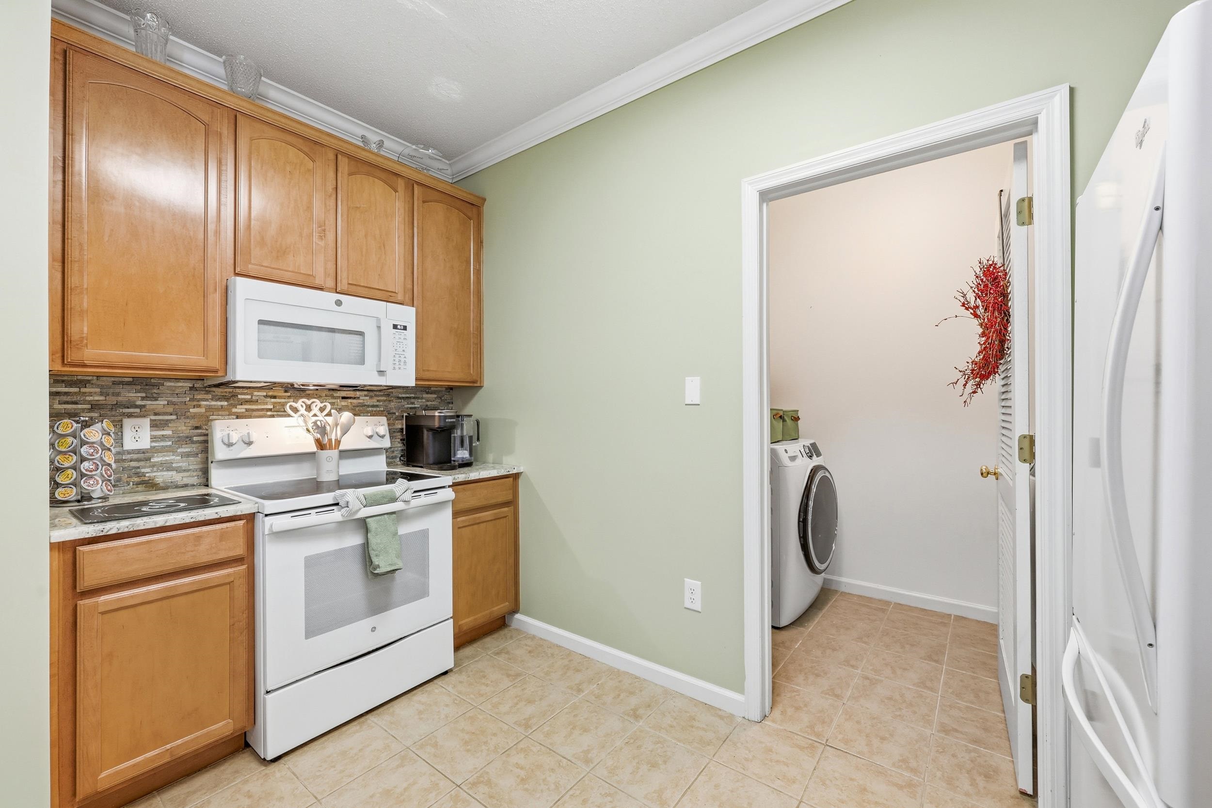 5870 Longwood Drive, Unit 203 Murrells Inlet, SC 29576 - Photo 12 of 32 Kitchen featuring white appliances, backsplash, washer / clothes dryer, ornamental molding, and brown cabinets