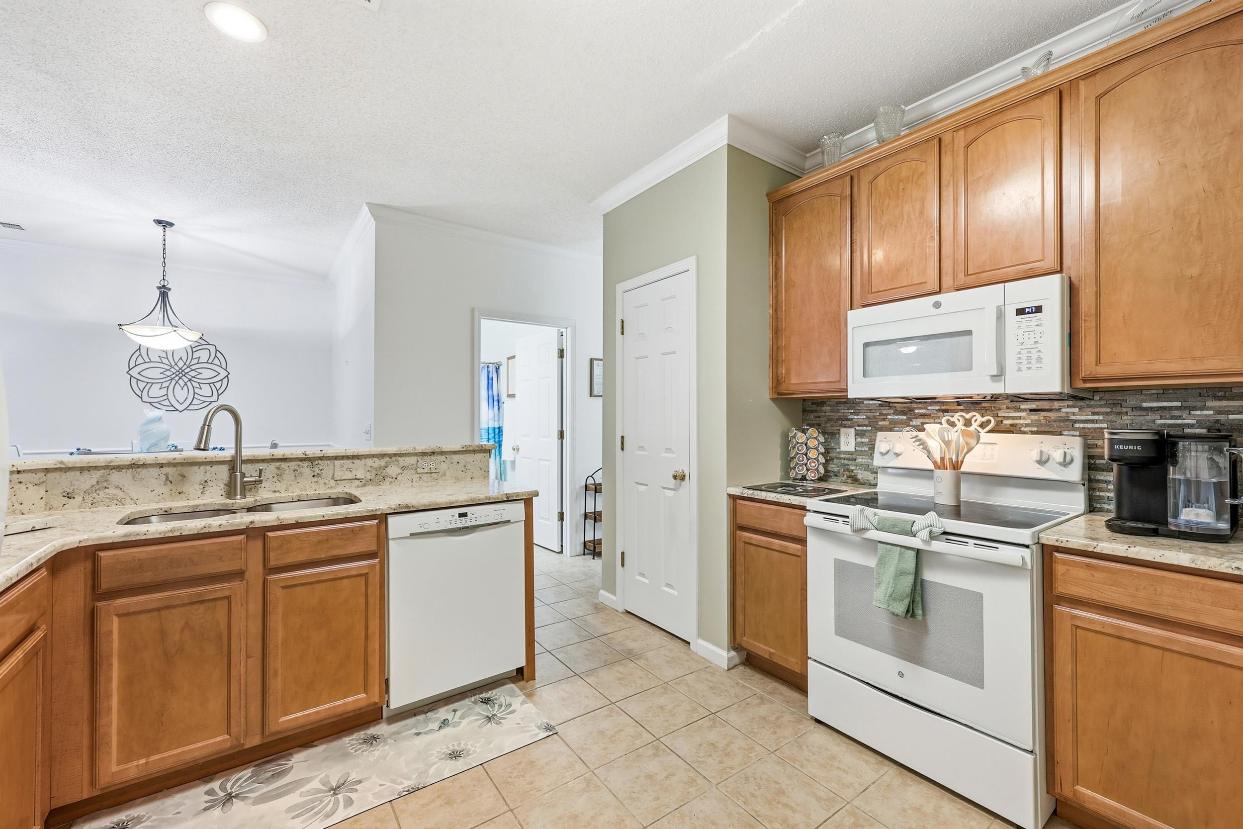 5870 Longwood Drive, Unit 203 Murrells Inlet, SC 29576 - Photo 10 of 32 Kitchen with white appliances, brown cabinets, decorative light fixtures, light stone countertops, and crown molding