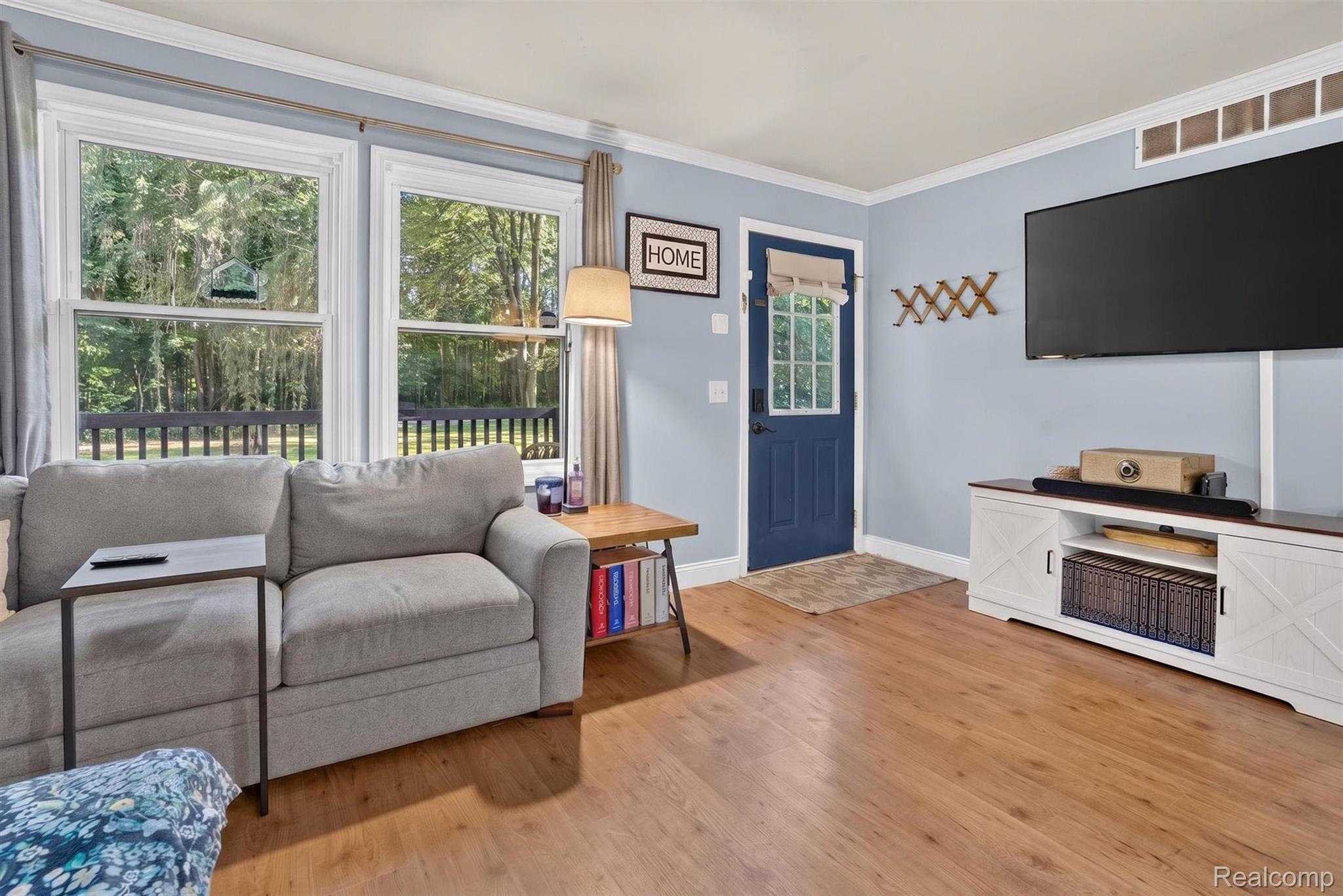 8696 West Sargent Road Fowlerville, MI 48836 - Photo 6 of 36 Living room featuring wood-finish flooring, two large windows, a blue paneled door with a window, and a white media console with dark wood top