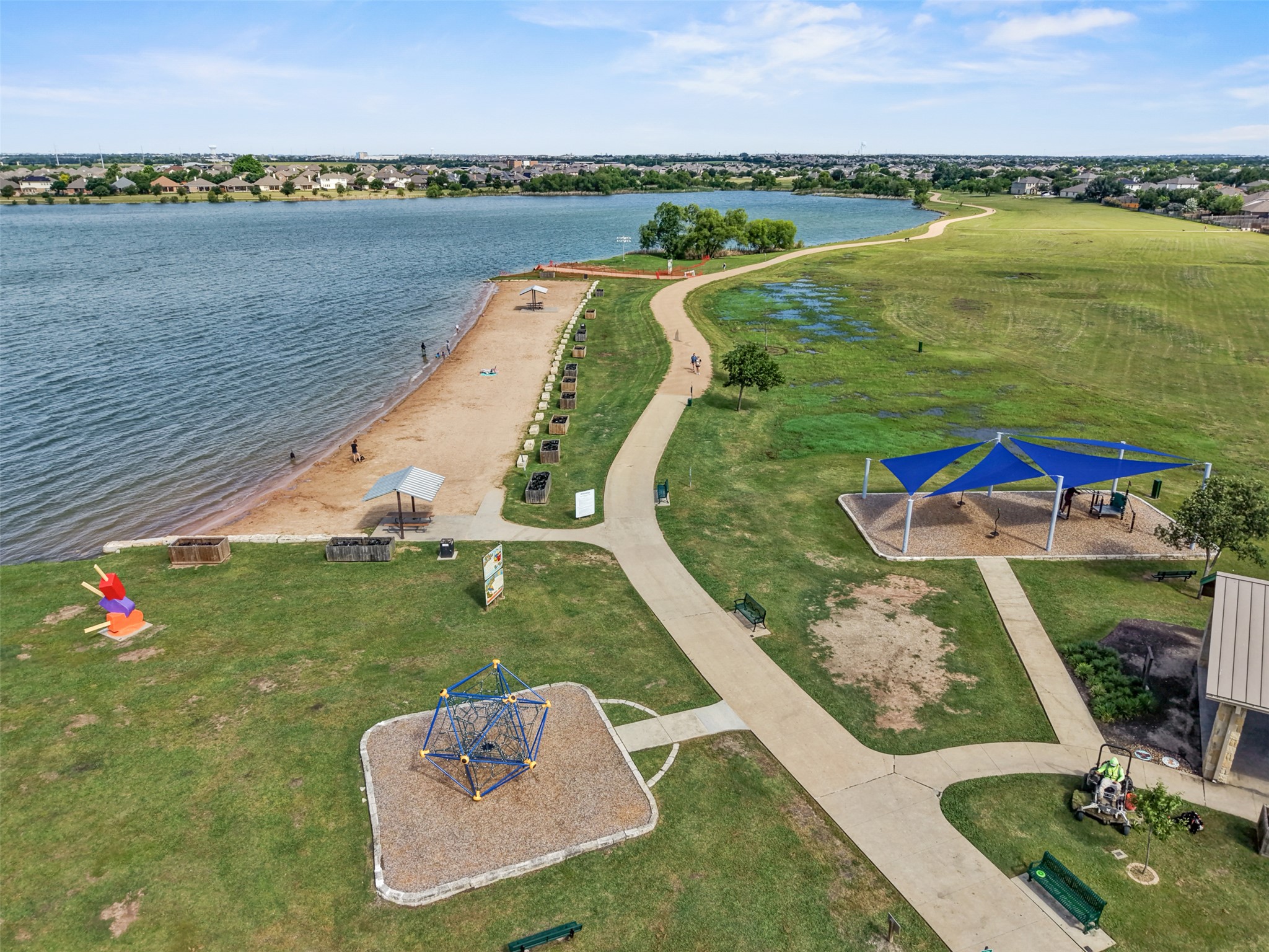 2521 Amen Corner Road Pflugerville, TX 78660 - Photo 39 of 40 Expansive lakeside park with a sandy beach area, paved walking paths, multiple shaded structures, and playground equipment set on wood chip surfacing