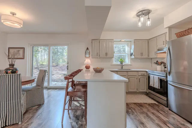 a kitchen with a refrigerator a sink dishwasher a stove and a dining table with wooden floor