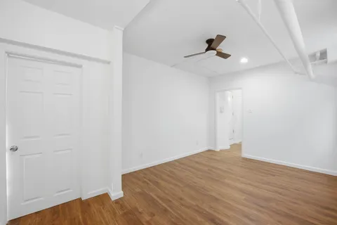 an empty room with wooden floor ceiling fan and windows