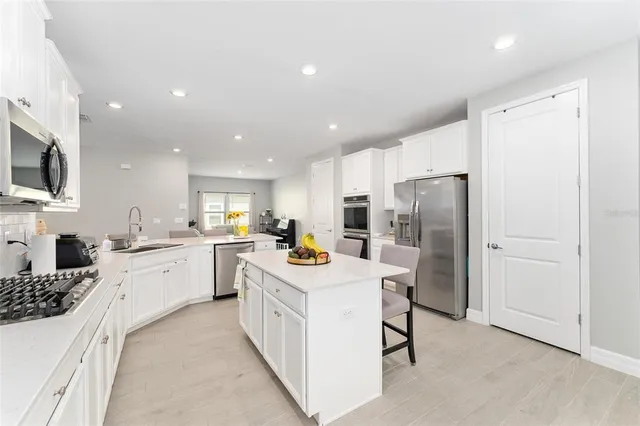 a kitchen with stainless steel appliances granite countertop a sink a stove a dining table and chairs with white cabinets