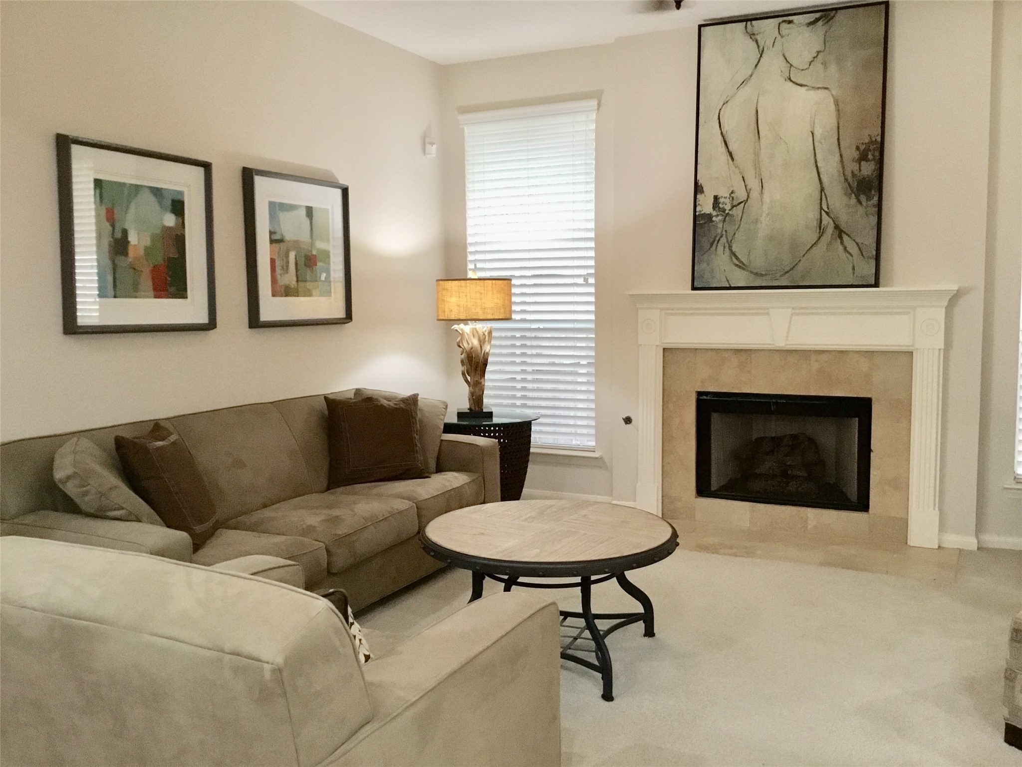 3 North Spiral Vine Circle Spring, TX 77381 - Photo 17 of 41 A cozy living room featuring a stone fireplace and neutral carpet. It includes a comfortable sofa, a matching armchair, and a round coffee table. Artwork adorns the walls, and a tall window with blinds allows natural light to brighten the space.
