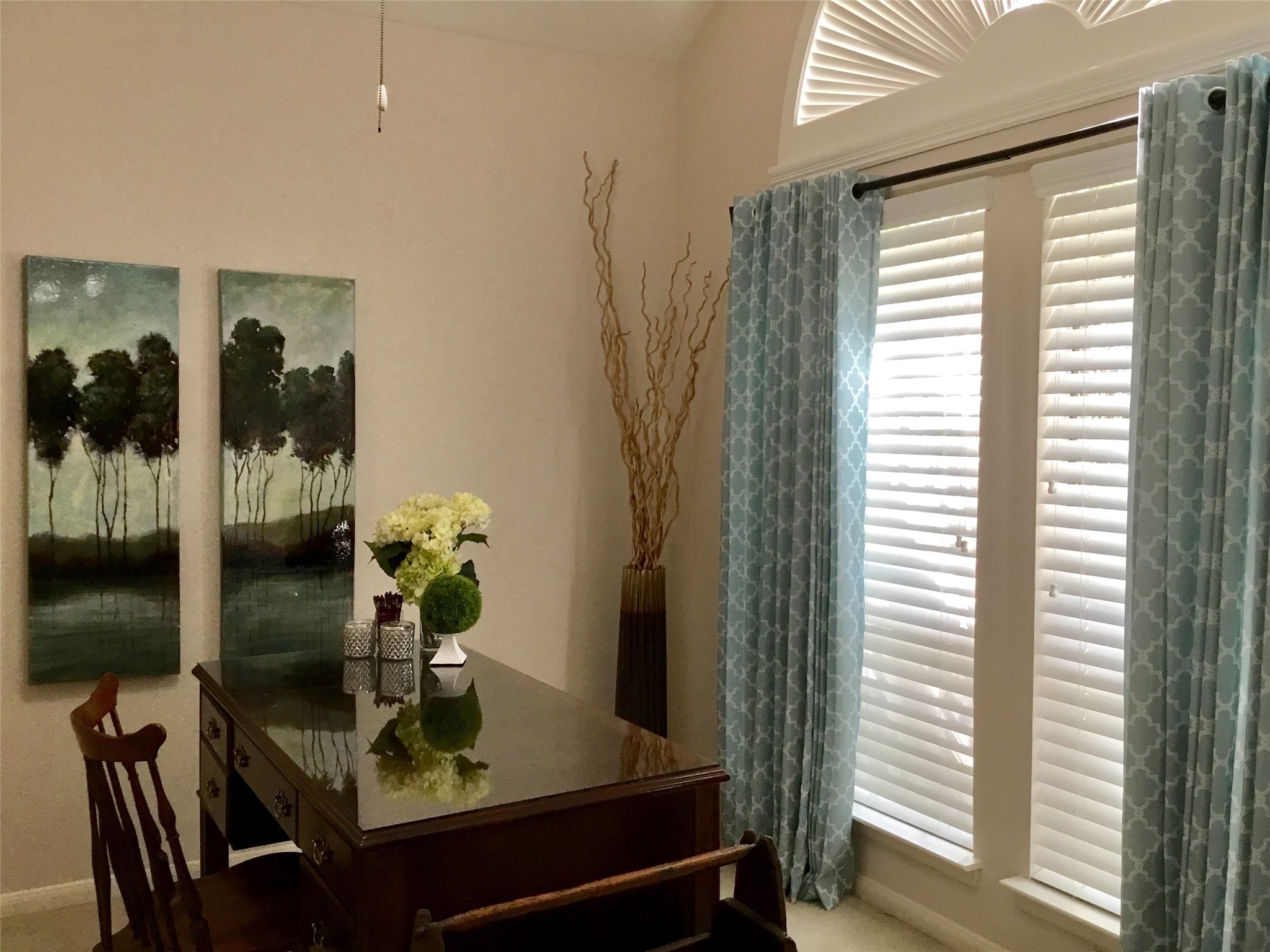 3 North Spiral Vine Circle Spring, TX 77381 - Photo 30 of 41 This bright room features a high ceiling with elegant arched windows, adorned with patterned blue curtains. It includes a classic wooden desk and chair set, complemented by tasteful wall art and decor. Perfect for a home office or study area.