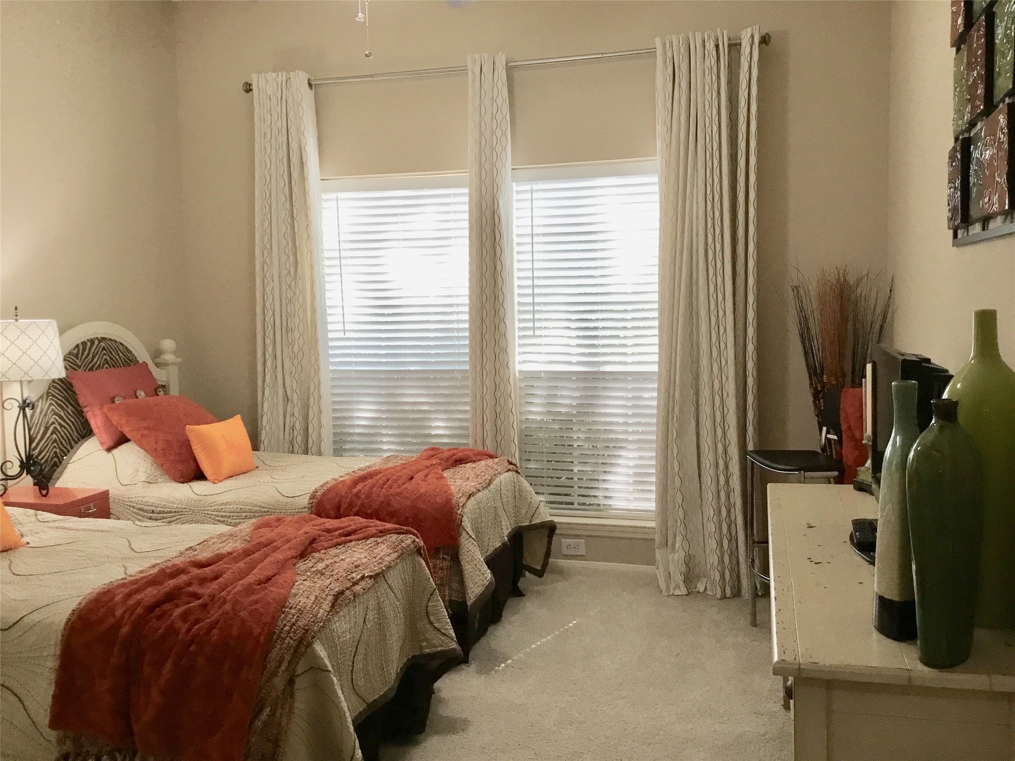 3 North Spiral Vine Circle Spring, TX 77381 - Photo 34 of 41 This cozy bedroom features two twin beds with elegant bedding and vibrant accent pillows. Natural light filters through large windows with stylish curtains. The room is complemented by a dresser with decorative vases and neutral-toned walls, creating a warm and inviting atmosphere.