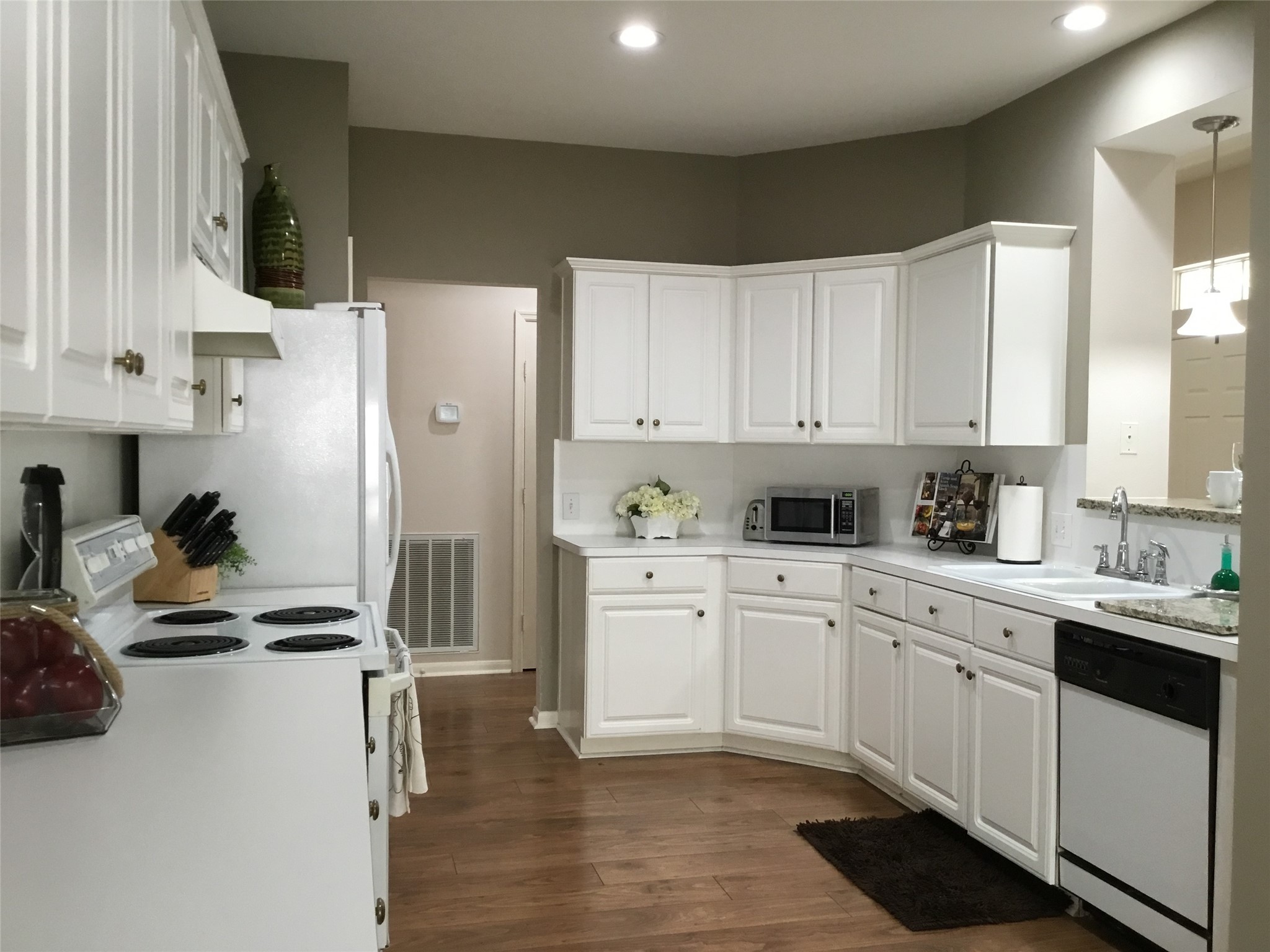 3 North Spiral Vine Circle Spring, TX 77381 - Photo 6 of 41 This kitchen features white cabinetry, wood flooring, and modern appliances, including a stove, dishwasher, and microwave. It has a cozy layout with ample counter space and overhead lighting, creating a bright and inviting atmosphere.