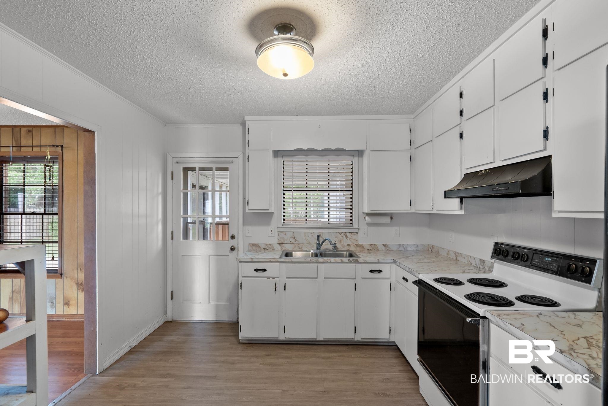 716 North Cedar Street Foley, AL 36535 - Photo 11 of 25 Kitchen featuring white cabinetry, light-toned countertops, a stainless steel sink, and wood-finish flooring