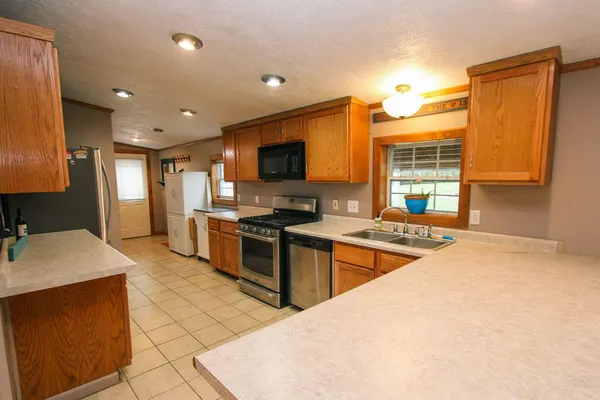 a open kitchen with stainless steel appliances granite countertop a stove top oven a sink a dining table and chairs with wooden floor