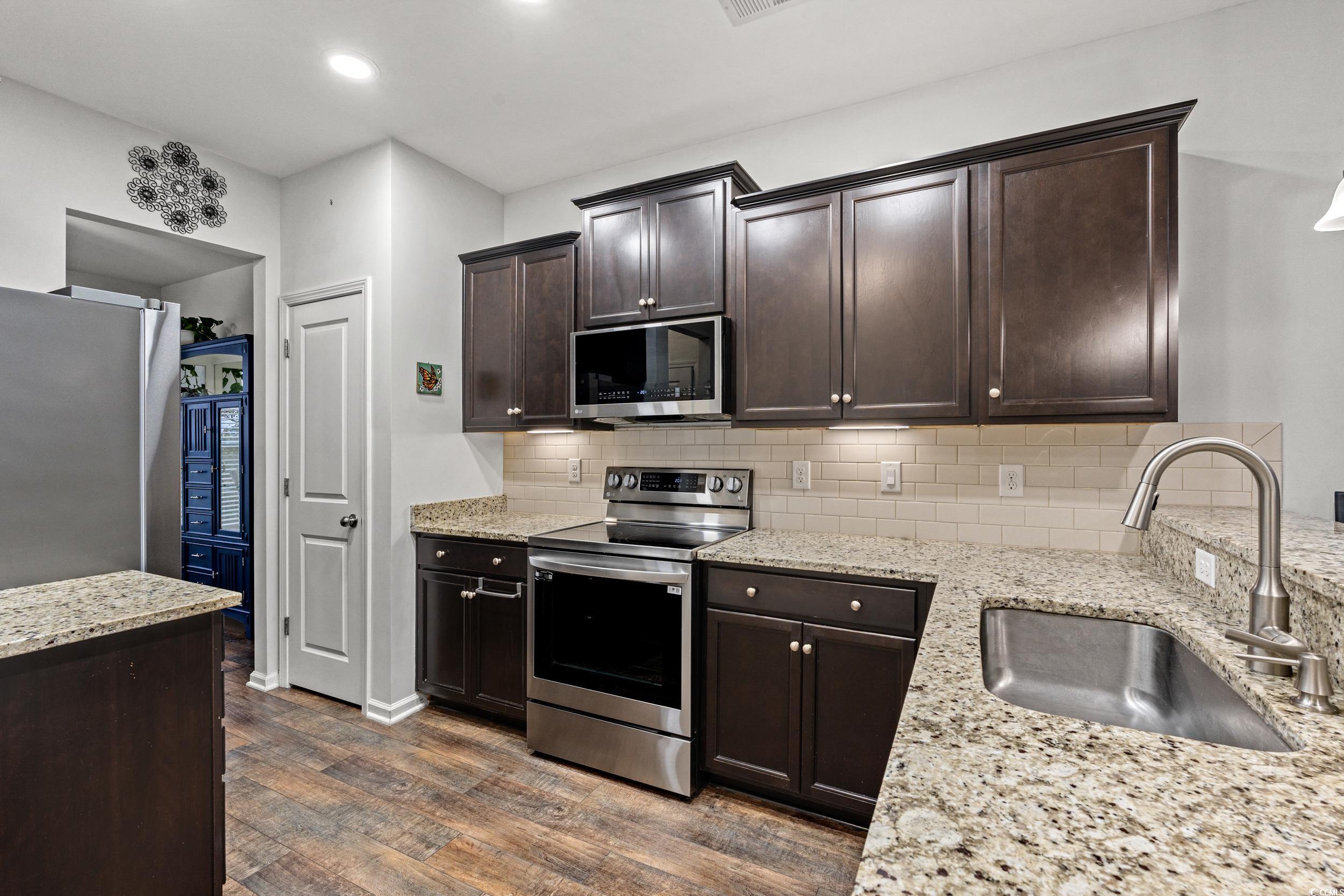 306 Castle Drive, Unit 306 Myrtle Beach, SC 29579 - Photo 11 of 30 Kitchen featuring dark brown cabinets, appliances with stainless steel finishes, light stone counters, dark wood-style floors, and backsplash