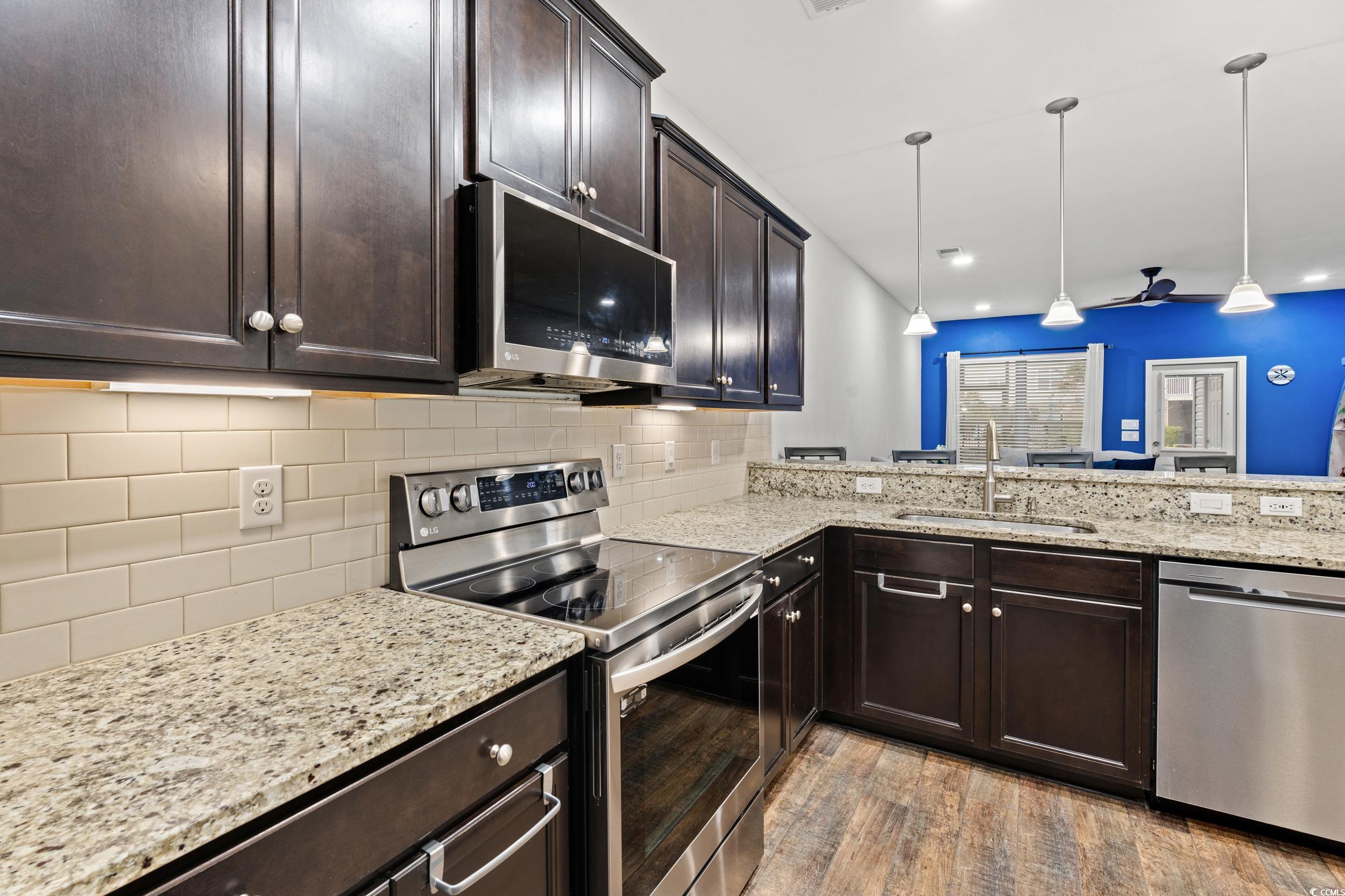 306 Castle Drive, Unit 306 Myrtle Beach, SC 29579 - Photo 10 of 30 Kitchen featuring stainless steel appliances, dark brown cabinetry, light stone counters, pendant lighting, and light wood-type flooring