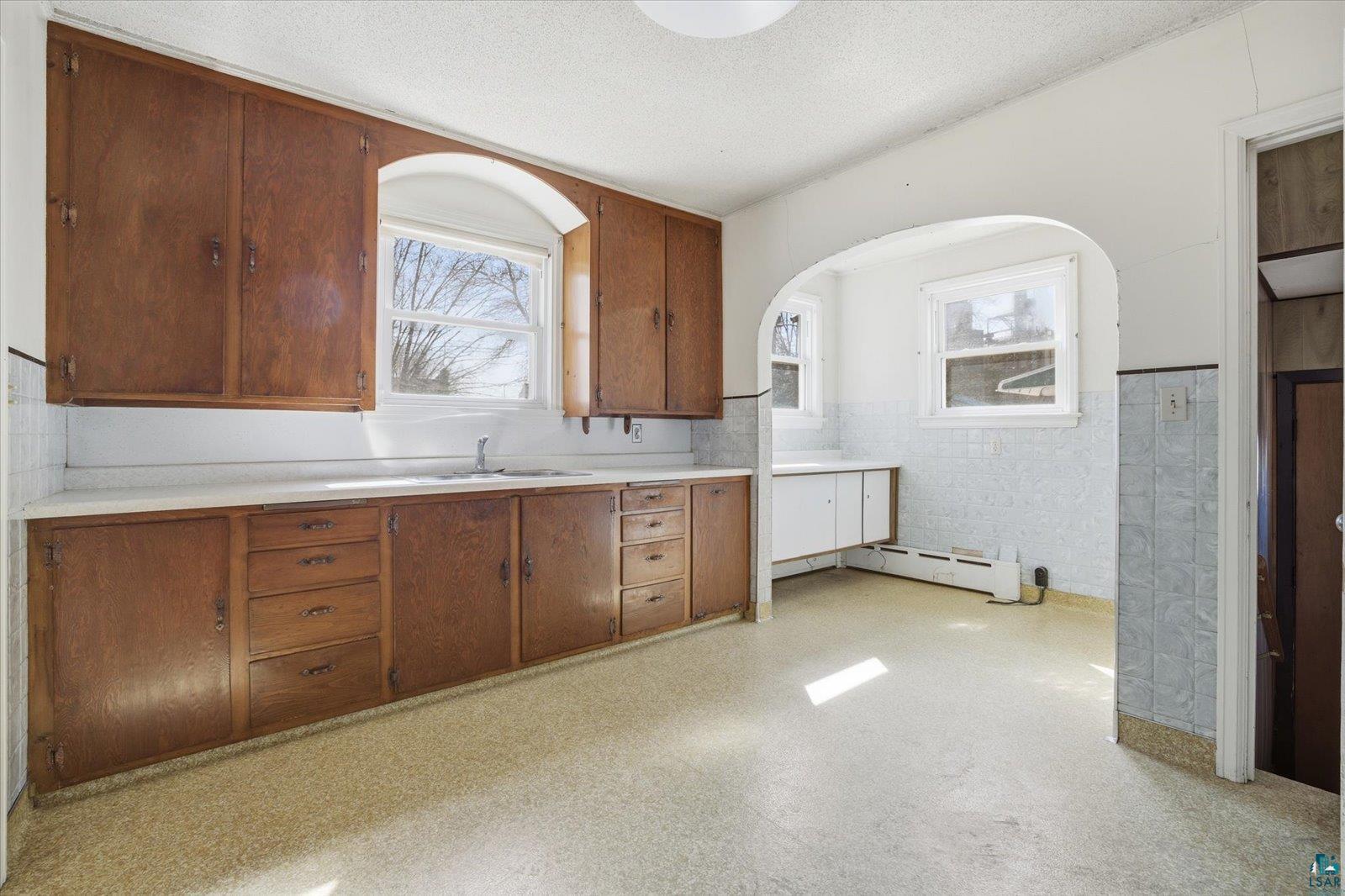 709 Michigan Street Hibbing, MN 55746 - Photo 7 of 47 Kitchen featuring light countertops, wood finish cabinets, light floors, a wainscoted wall, and tile walls