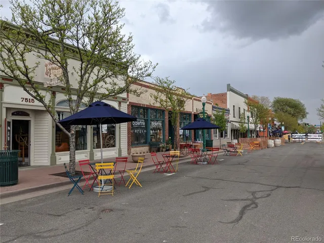 a view of a street with tables and chairs under an umbrella