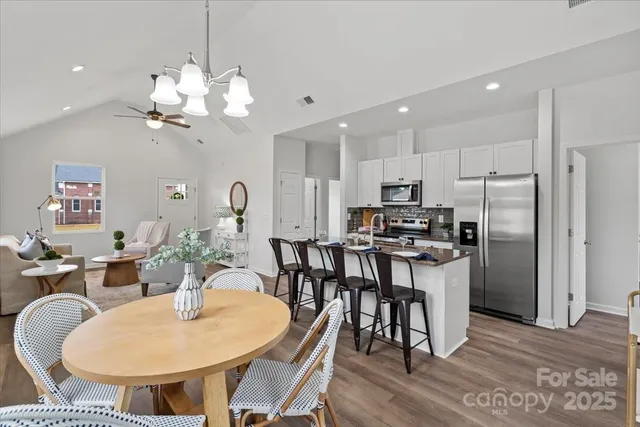 a kitchen with stainless steel appliances kitchen island granite countertop a dining table chairs and a refrigerator