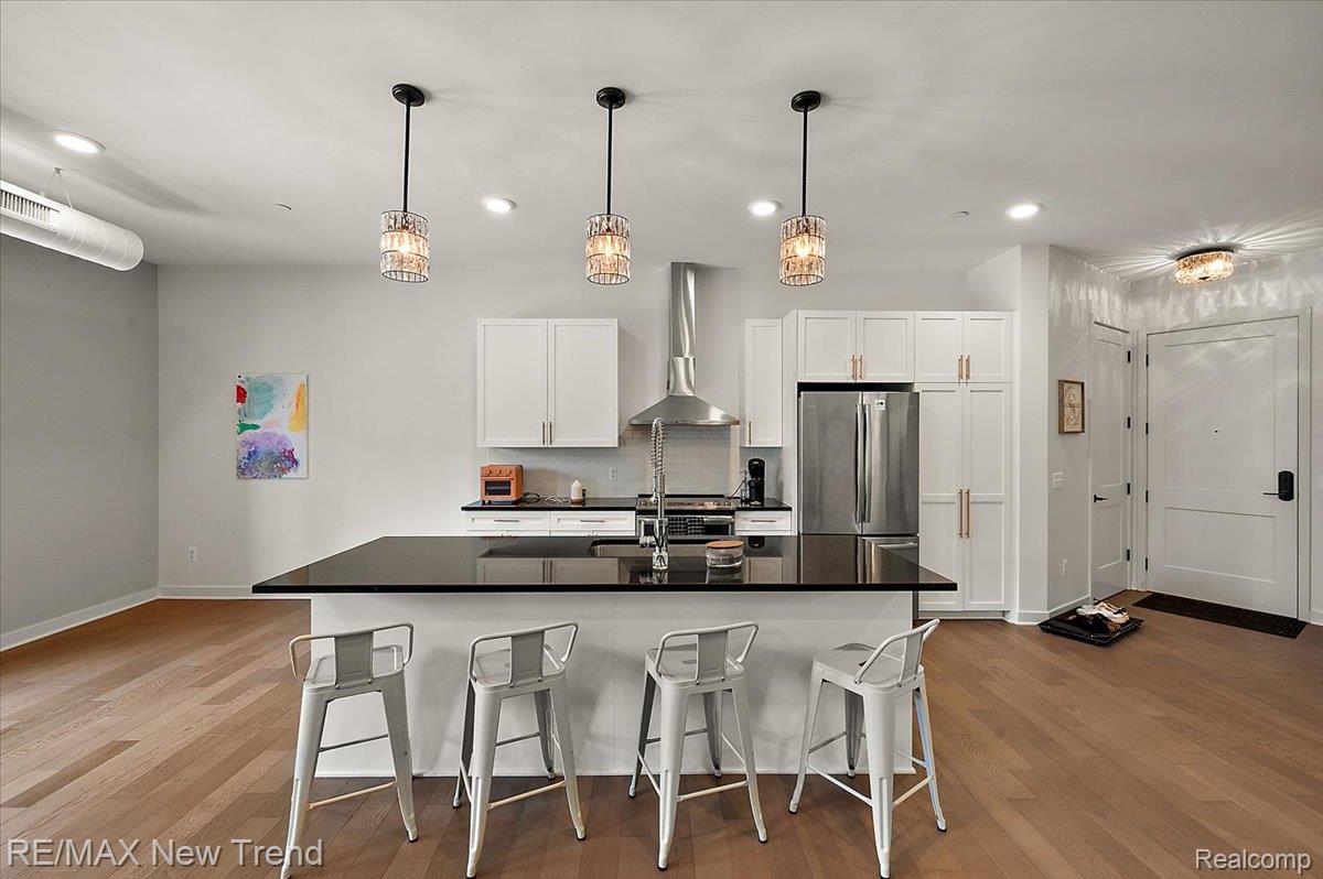 804 North Main Street, Unit 2H Rochester, MI 48307 - Photo 15 of 52 Open concept living space featuring wood-finish flooring, white cabinetry, a kitchen island with a dark countertop, stainless steel appliances, and pendant lighting