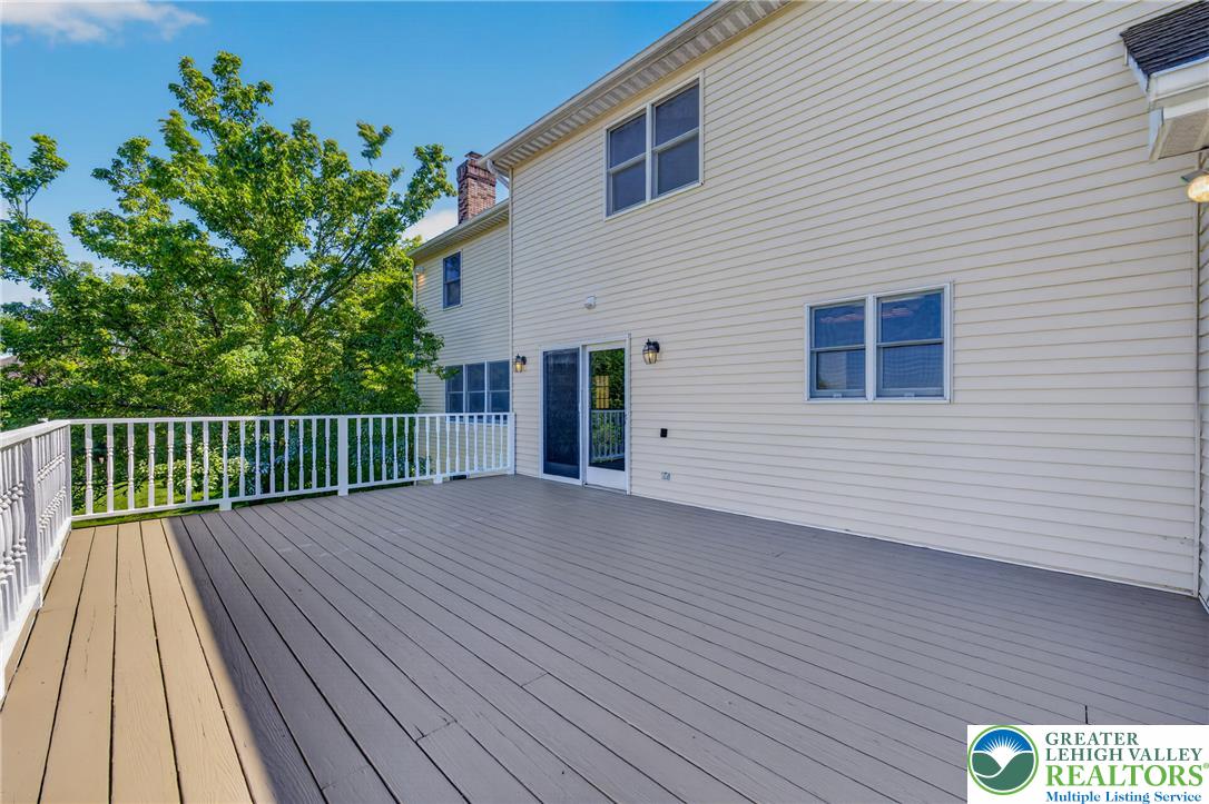 630 Clearfield Road Nazareth, PA 18064 - Photo 89 of 100 An elevated wood deck with white railings overlooks mature green trees under a clear blue sky.