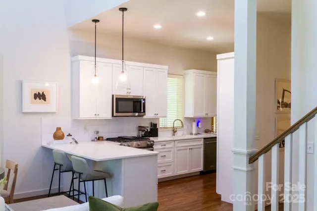 a kitchen with stainless steel appliances a stove a sink dishwasher a microwave oven a dining table and chairs with wooden floor