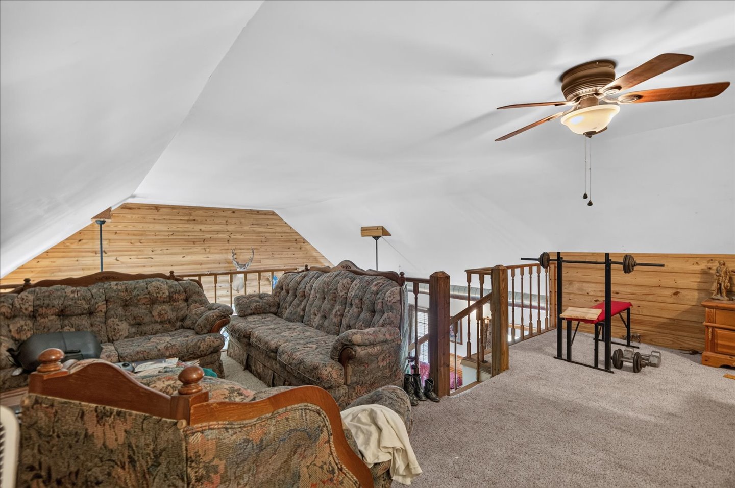 26115 4157th Road Nowata, OK 74048 - Photo 22 of 36 Sloped ceiling design, wood plank wall accent, carpeted flooring, wood baluster railing, and a ceiling fan with integrated lighting
