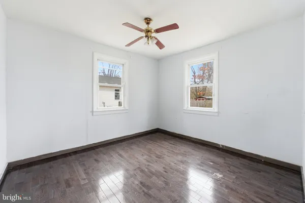 an empty room with wooden floor ceiling fan and windows
