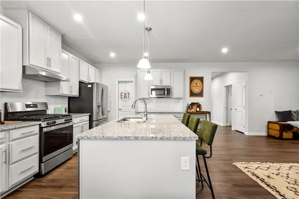 a kitchen with stainless steel appliances granite countertop a refrigerator a stove a sink a dining table and chairs with wooden floor