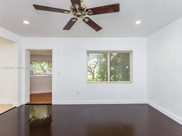 an empty room with wooden floor chandelier fan and windows