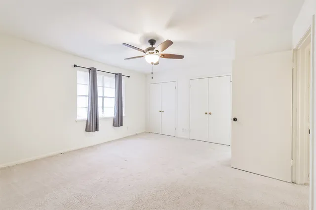 an empty room with chandelier fan and windows