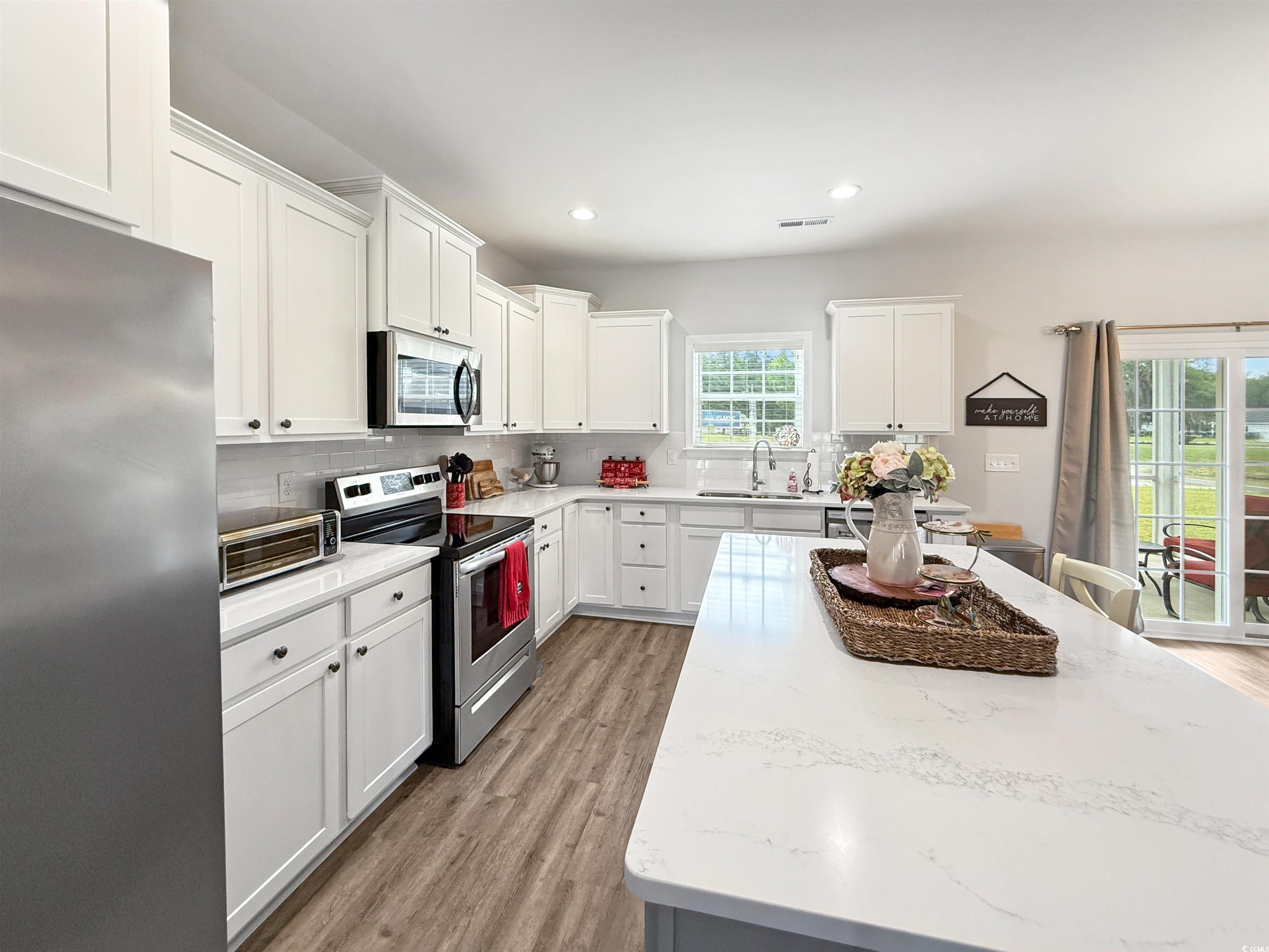 40 Little Peru Court Georgetown, SC 29440 - Photo 10 of 32 Kitchen with appliances with stainless steel finishes, a sink, light wood-type flooring, decorative backsplash, and white cabinetry