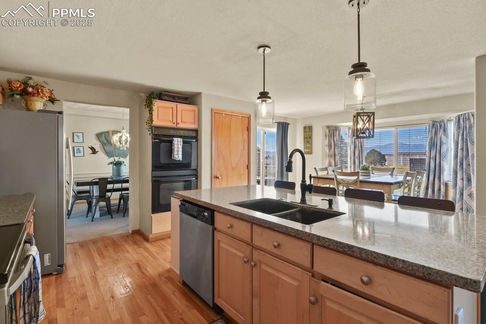 7660 Bullet Road Peyton, CO 80831 - Photo 11 of 50 Kitchen featuring a chandelier, hanging light fixtures, light wood finished floors, stainless steel appliances, and a center island with sink