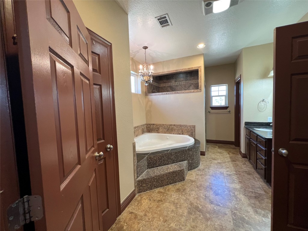 665 Wilson Road Red Rock, TX 78662 - Photo 21 of 34 Full bathroom with a bath, a textured ceiling, healthy amount of natural light, vanity, and a chandelier
