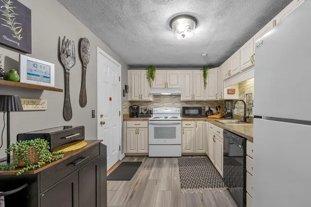 a kitchen with stainless steel appliances granite countertop a refrigerator a stove a sink dishwasher and white cabinets with wooden floor